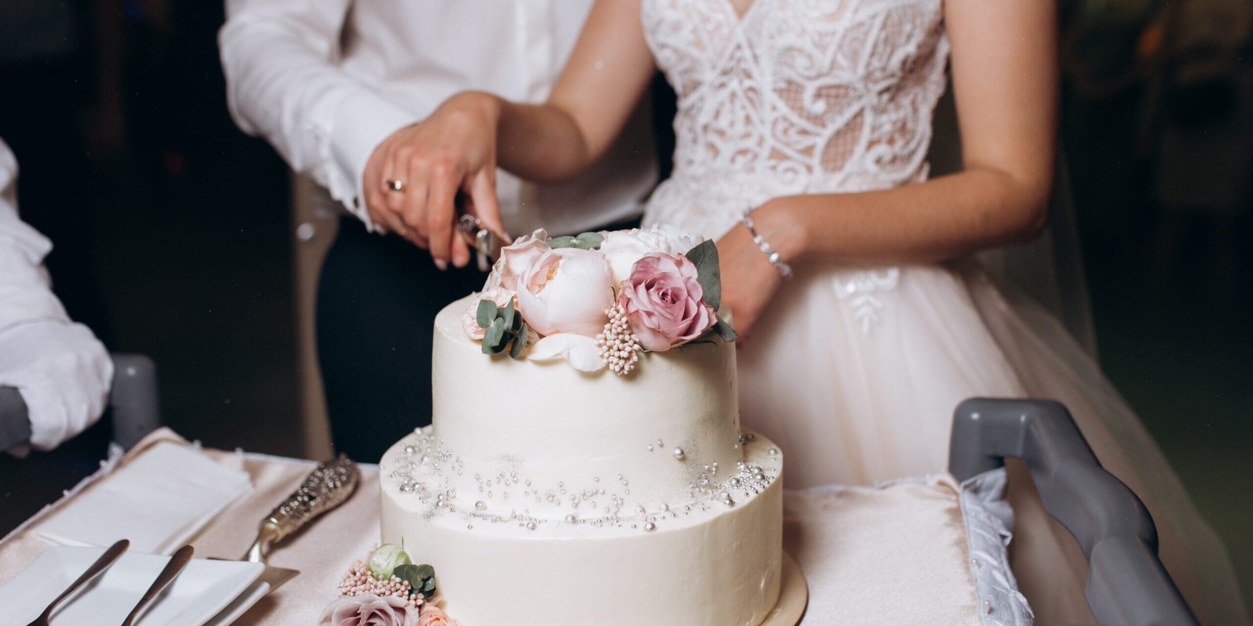 Bride and groom are cutting decorated with flowers wedding cake